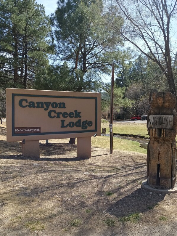 A sign for Canyon Creek Lodge with a wooden bear sculpture nearby.