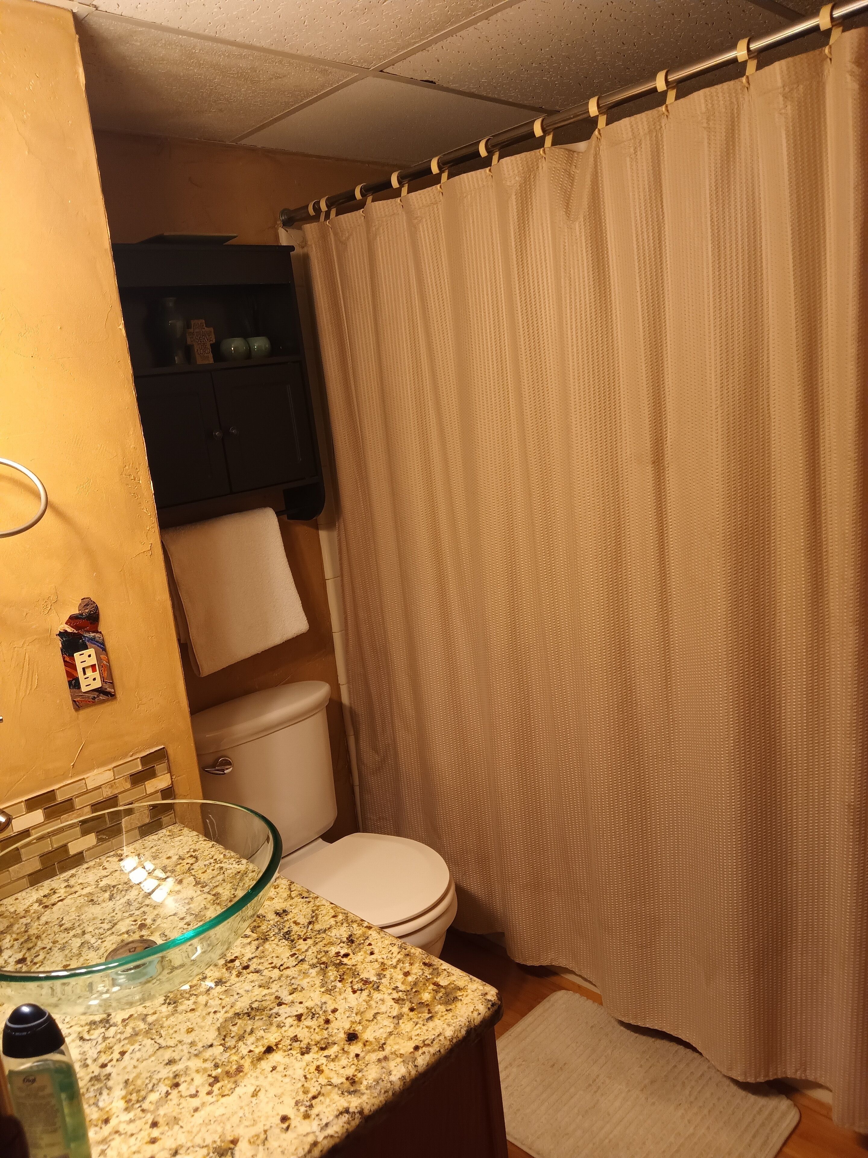 Un baño con lavamanos de vidrio, inodoro y cortina de ducha color beige.