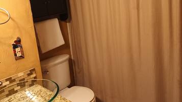 Un baño con lavamanos de vidrio, inodoro y cortina de ducha color beige.