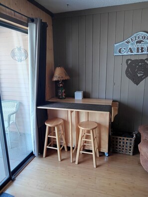 A cozy room with a wooden bar area, two stools, a lamp, and a bear-themed wall decoration. - Charming 1-bedroom condo in superb Ruidoso with WiFi, AC (Ruidoso)