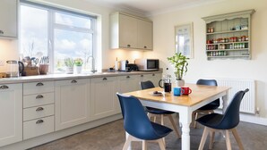 A modern kitchen with white cabinets, a wooden dining table, and blue chairs. - Jewel in the Garden of England - Two bedrooms (Lyminge)