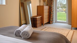 A bedroom with a bed, a dresser, a mirror, a wicker basket, and a view of the outdoors through a door. - Jewel in the Garden of England - Two bedrooms (Lyminge)