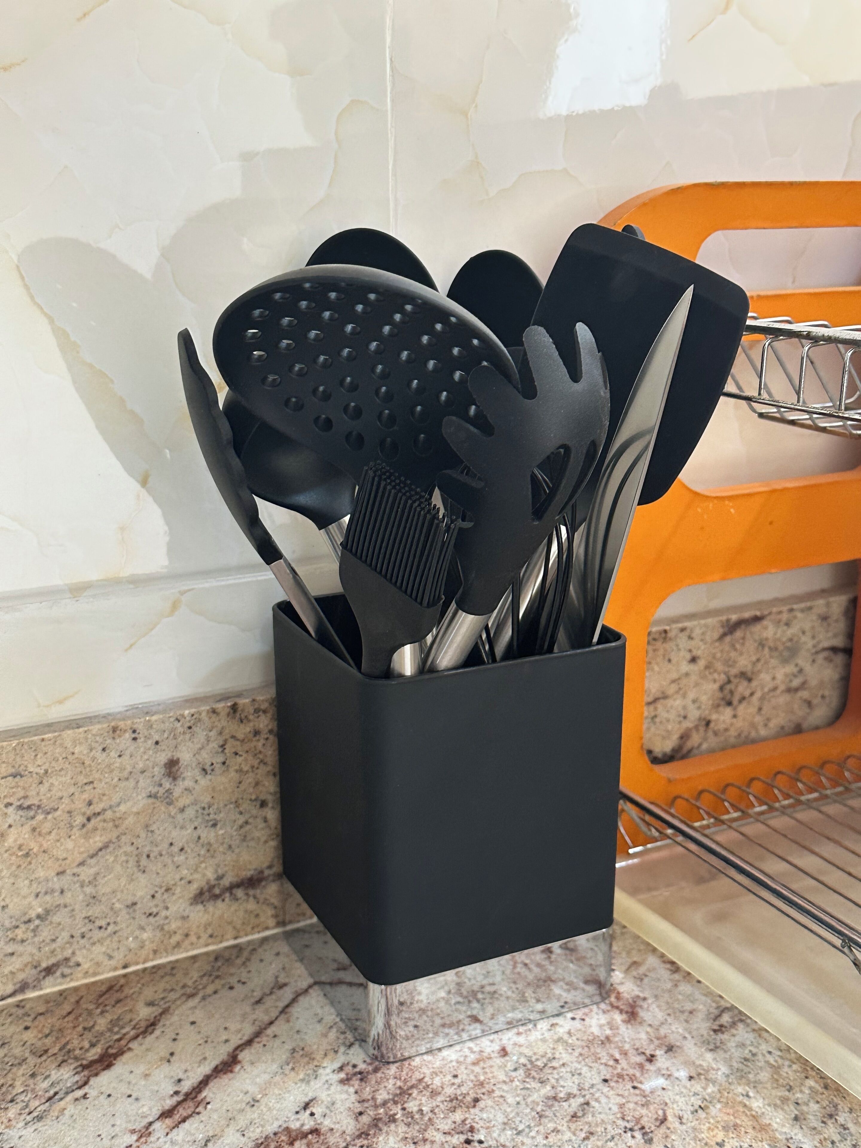 A black utensil holder with various kitchen tools on a kitchen counter.