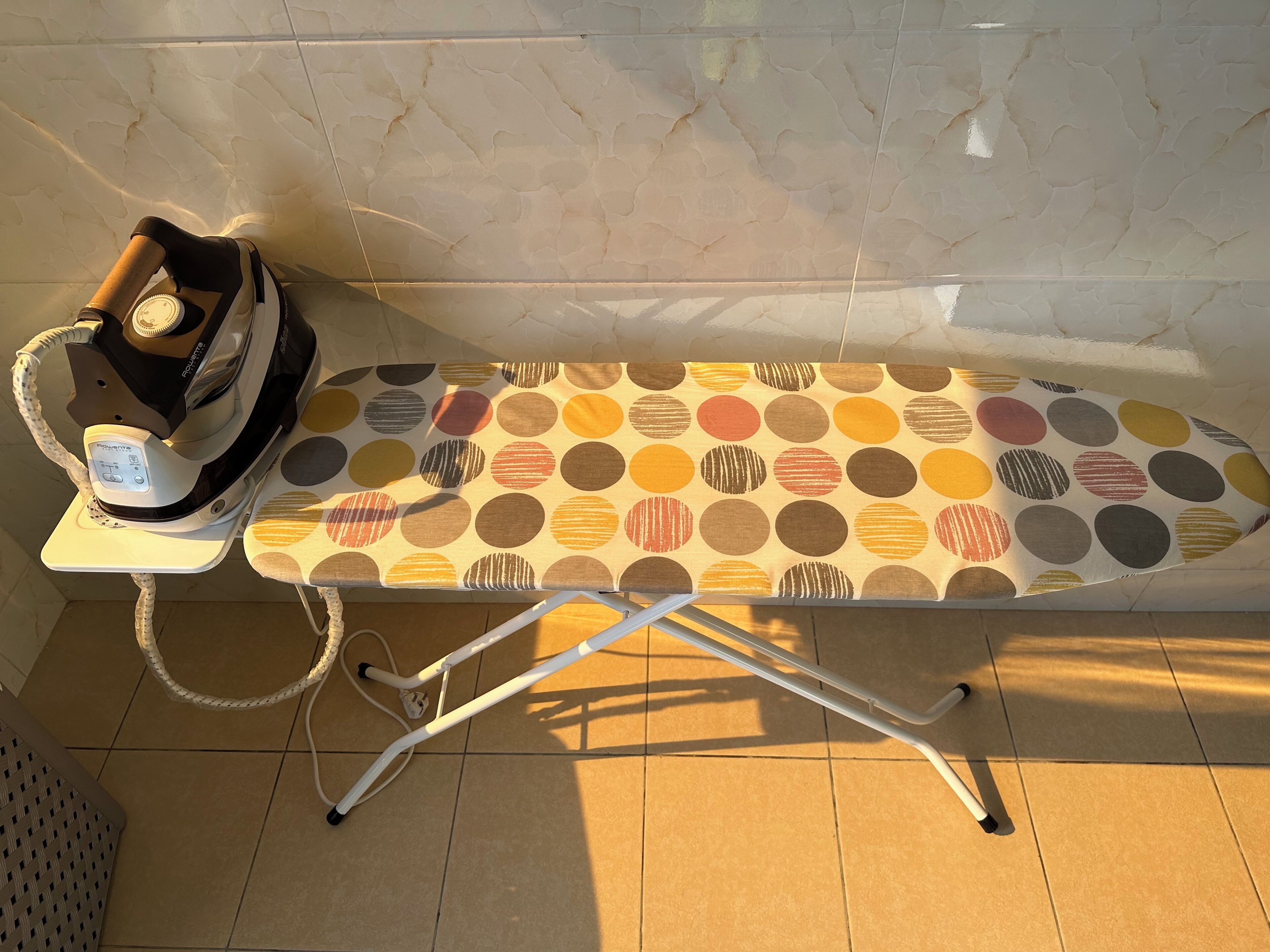 An ironing board with a polka dot cloth, an iron, and a white cable.