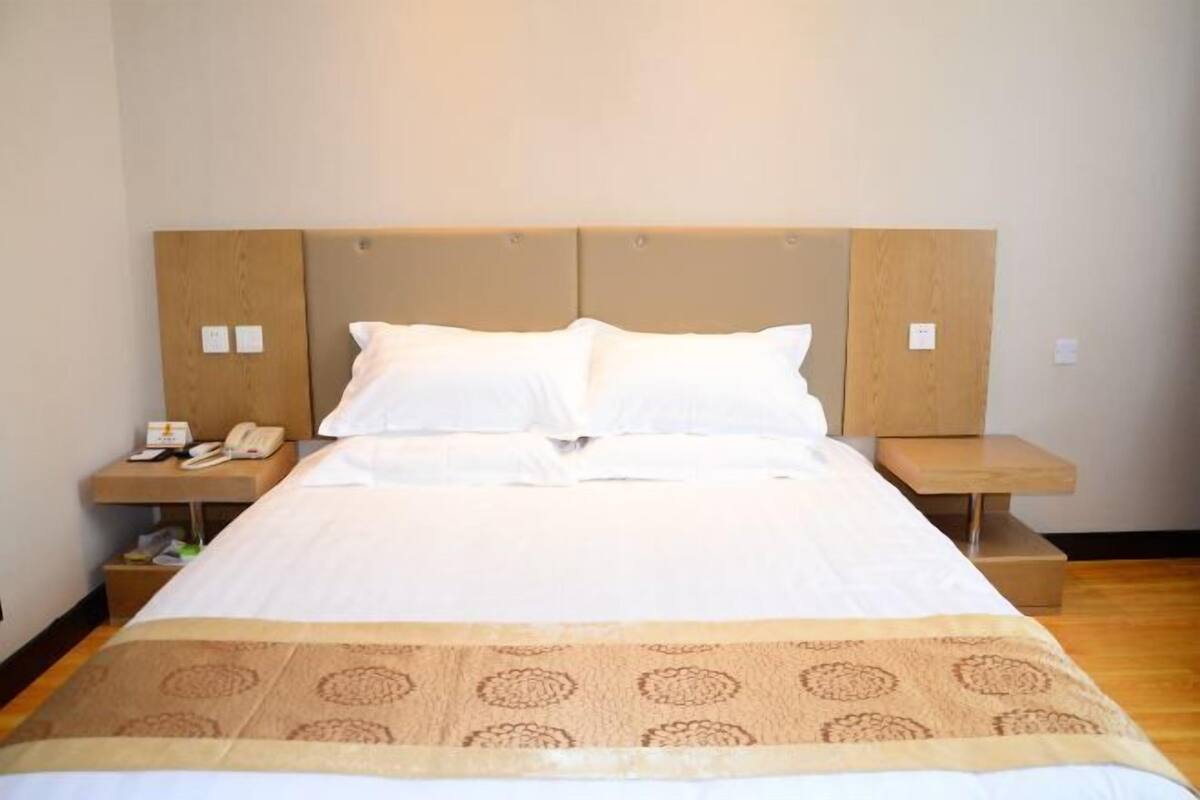A hotel room with a large bed, two bedside tables, a telephone, and a small nightstand.