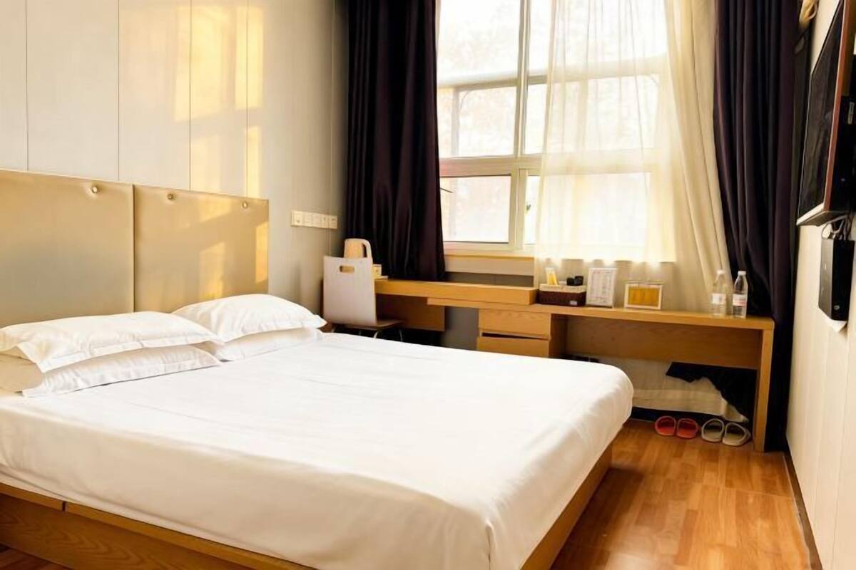 A hotel room with a bed, a desk, a chair, a window with curtains, and a TV.