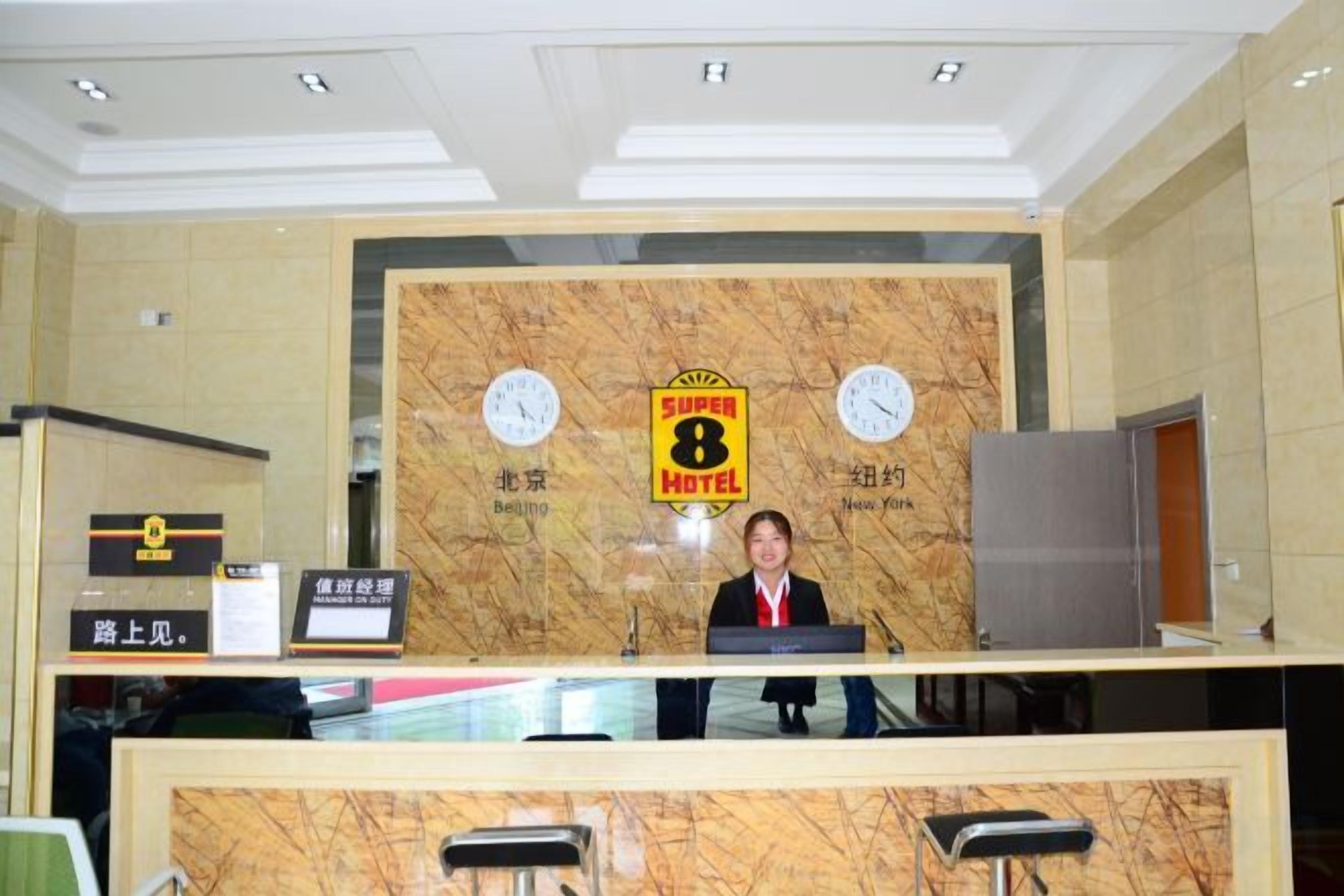 A hotel reception desk with a marble backdrop, clocks, and a sign indicating the hotel name.