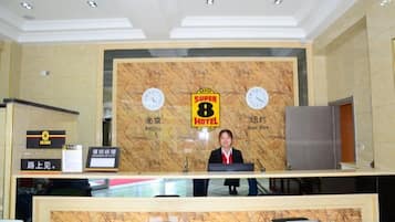 A hotel reception desk with a marble backdrop, clocks, and a sign indicating the hotel name.