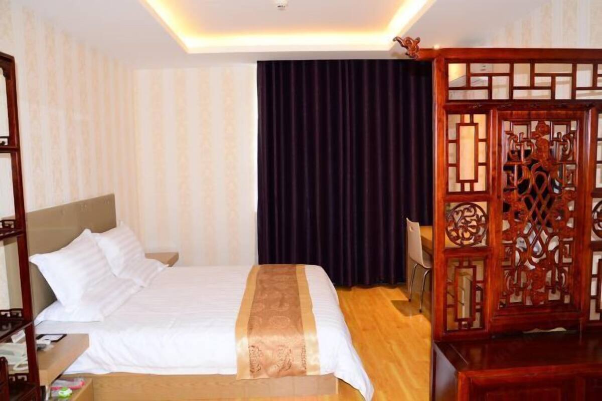 A hotel room with a bed, a desk, a chair, and a decorative wooden partition.