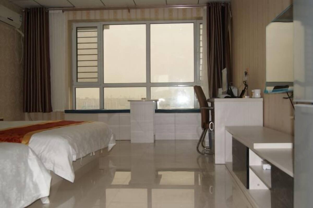 A hotel room with a bed, a desk, a chair, a mirror, and a window with curtains.