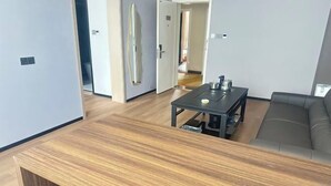 Moderni olohuone, jossa on puinen sohvapöytä, sohva sekä ruokailutila, jossa on pöytä ja tuolit.