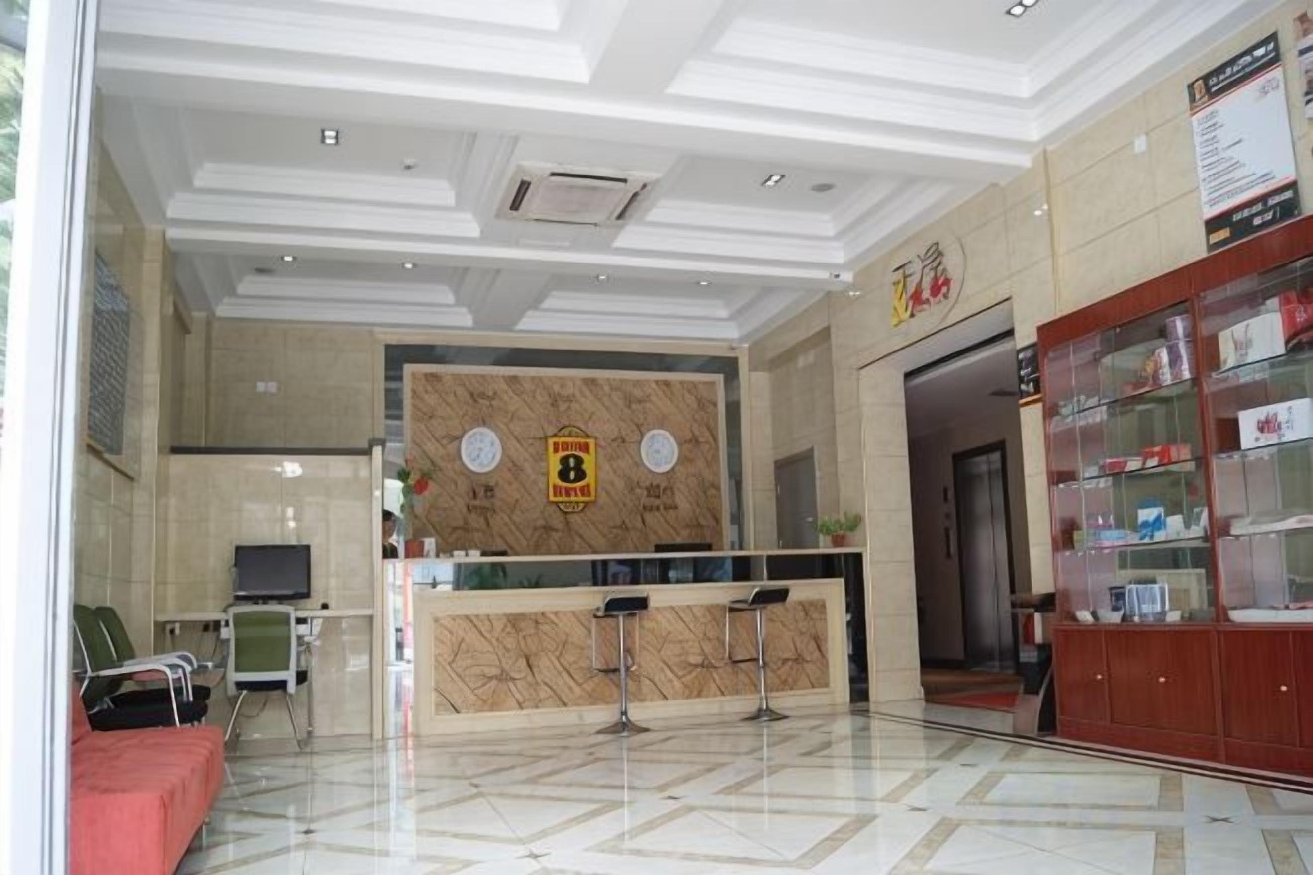 A hotel reception area with a marble floor, a reception desk, a waiting area with chairs, and a display cabinet with items.
