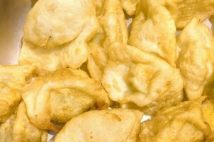 Primer plano de un alimento, probablemente una especie de pastel frito o albóndiga, con una capa exterior dorada.
