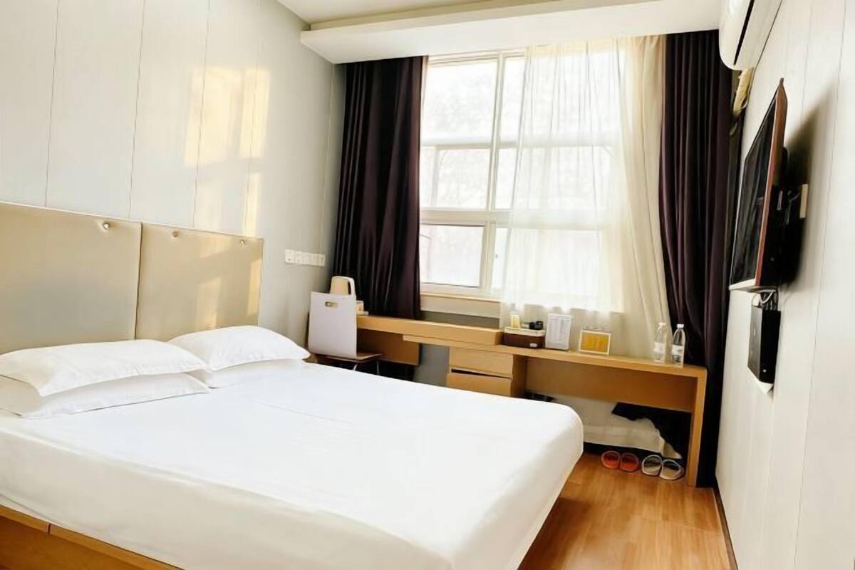 A hotel room with a bed, a desk, a chair, a TV, and a window with curtains.