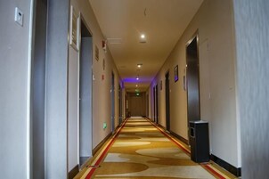 Pasillo de hotel con piso alfombrado, puertas a ambos lados y un bote de basura al final.