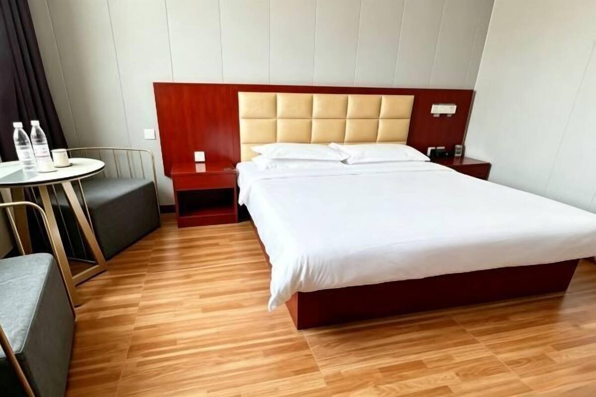 A hotel room with a large bed, a small round table with chairs, and a red nightstand.
