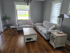 Een woonkamer met twee grijze banken, een witte salontafel, een klein bijzettafeltje, een vloerlamp en een potplant.