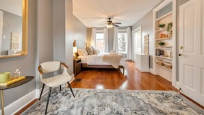 A bedroom with a bed, a chair, a nightstand, a bedside table, a ceiling fan, a window, and a bookshelf. - Downtown Lancaster Luxury 4BR - Garage & Parking (Lancaster)