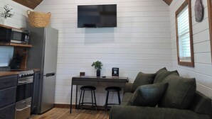 Cozinha compacta com eletrodomésticos modernos, área de refeições com banquetas e um espaço de estar aconchegante com sofá verde.
