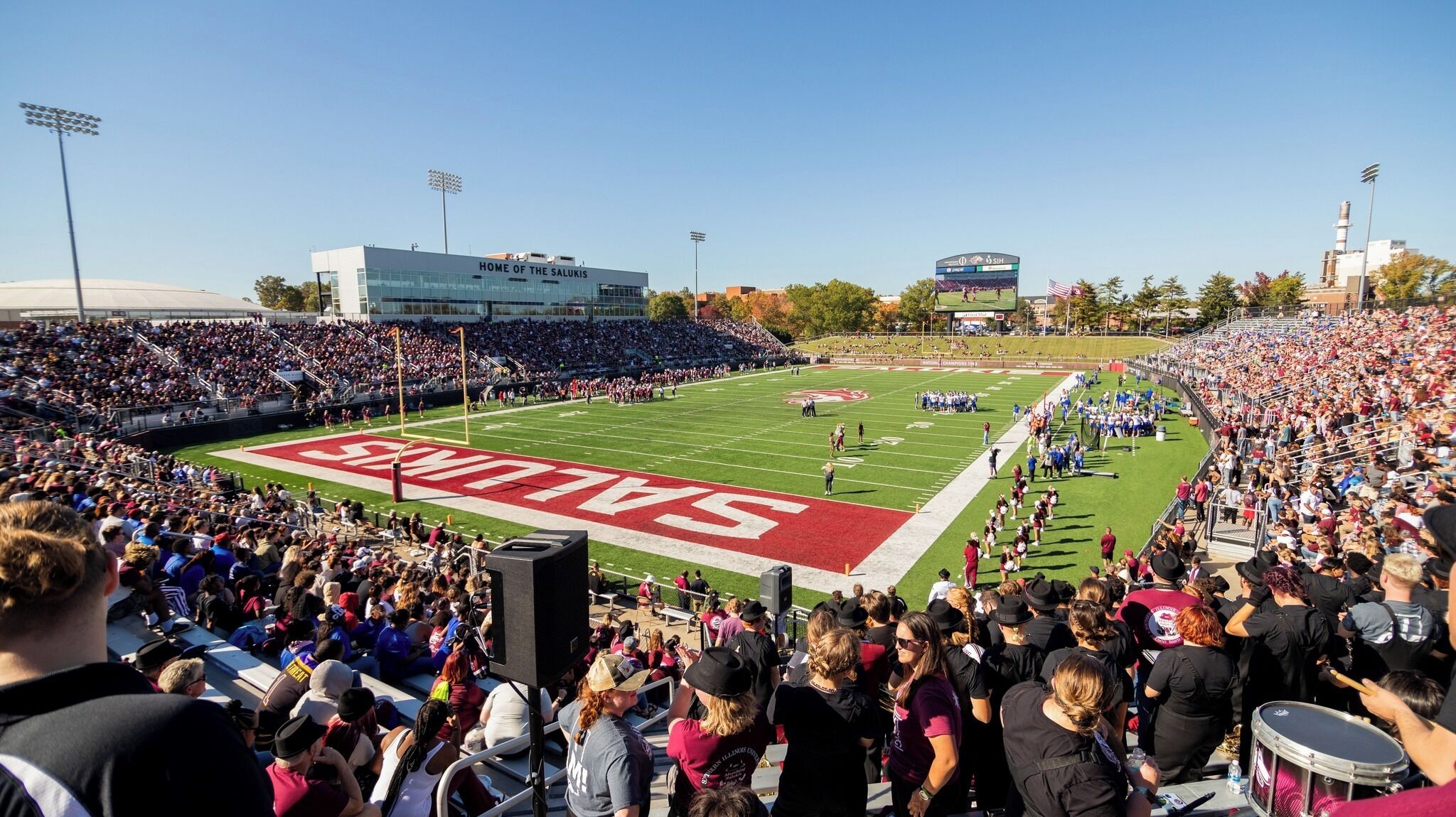 A stadium with a football field, bleachers, and a scoreboard.