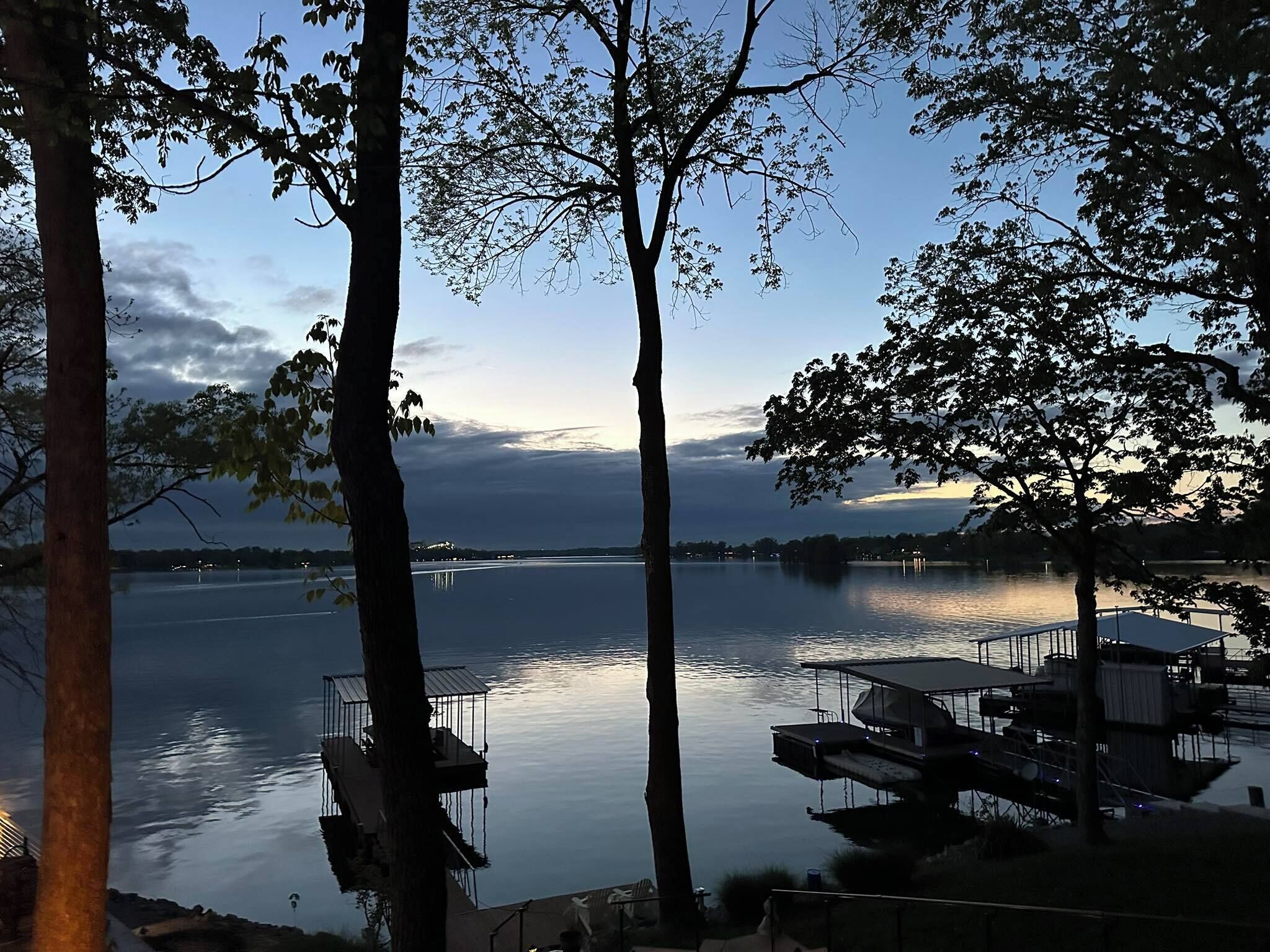 Vista de un lago con barcos amarrados, una superficie acuática tranquila y árboles que enmarcan la escena.
