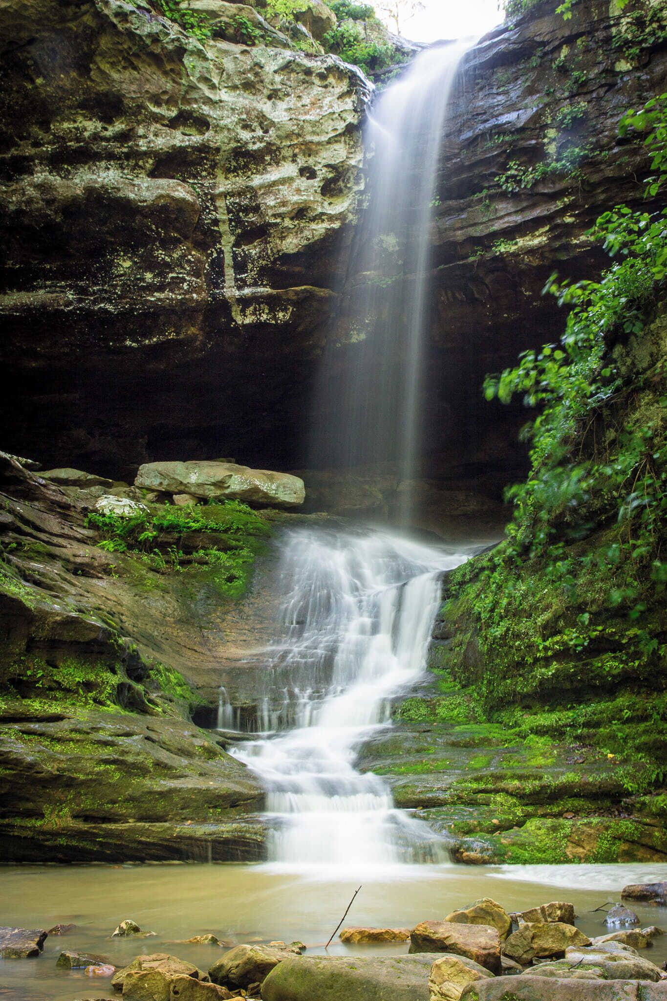 A waterfall cascading down a rocky cliff surrounded by lush greenery.