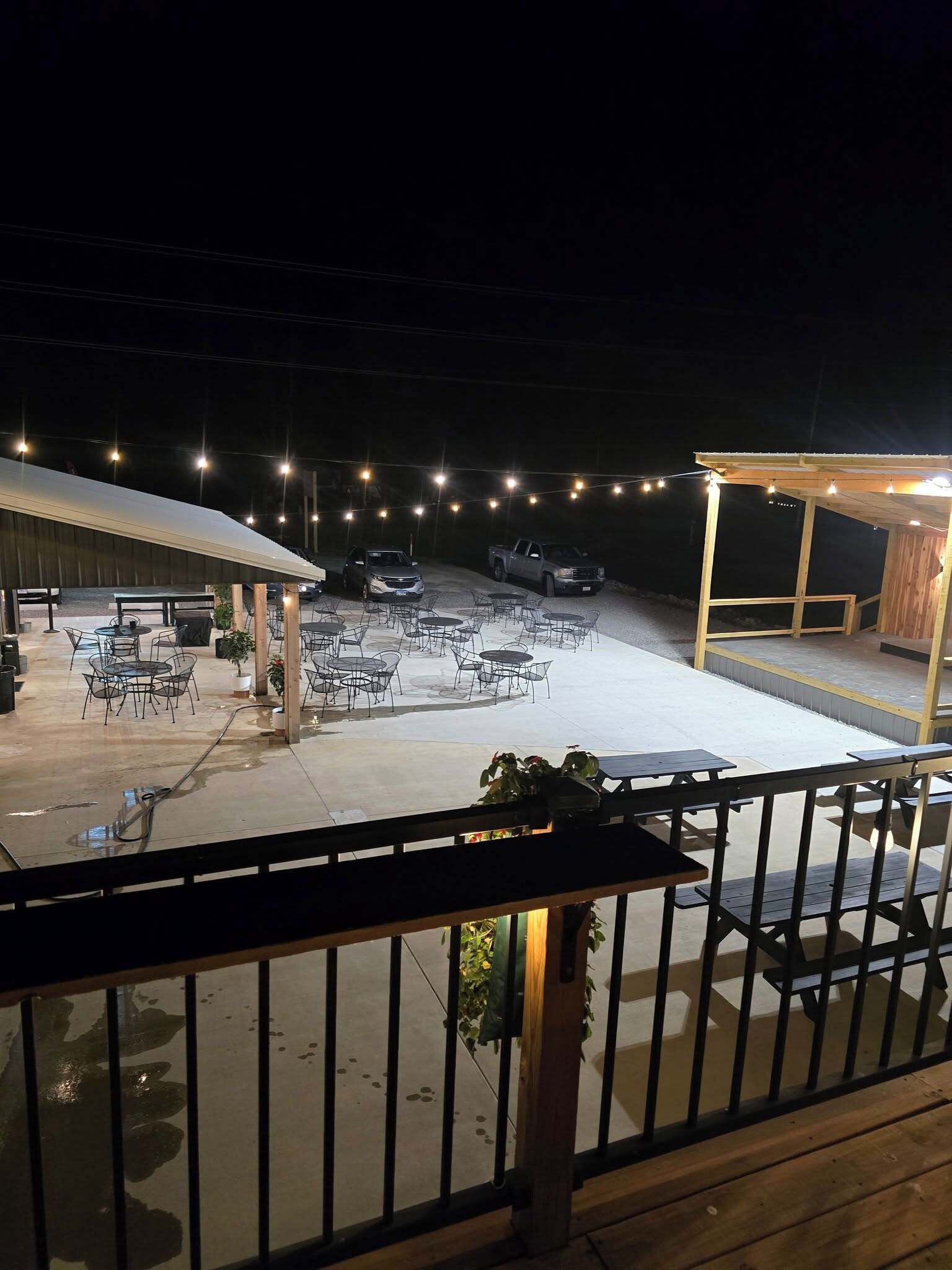 An outdoor patio area with tables and chairs, a covered seating area, and string lights.