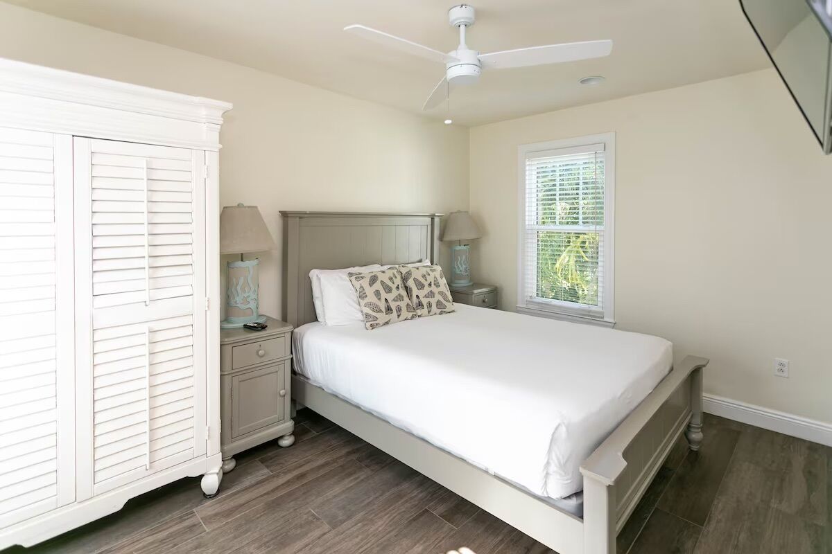A bedroom with a bed, nightstands, a wardrobe, a ceiling fan, and a window with blinds.