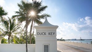 Un letrero blanco con la inscripción "DUCK KEY" sobre un puente, con palmeras y un cielo despejado.
