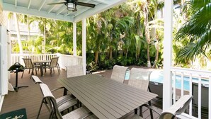 Un espacio comedor al aire libre cubierto con una mesa y sillas de madera, rodeado de exuberante vegetación tropical y una piscina.