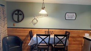 A dining area with a wooden wall, a 'Welcome' sign, a 'Country Kitchen' sign, and a cross decoration.