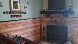 A living room with a stone fireplace, a mounted television, and a couch with a blanket.