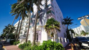 Un immeuble à plusieurs étages doté de balcons, de palmiers et d’un panneau indiquant une rue à sens unique.