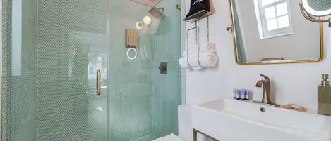 Un baño con cabina de ducha de vidrio, un inodoro blanco, un lavamanos con marco dorado y un espejo con marco dorado.