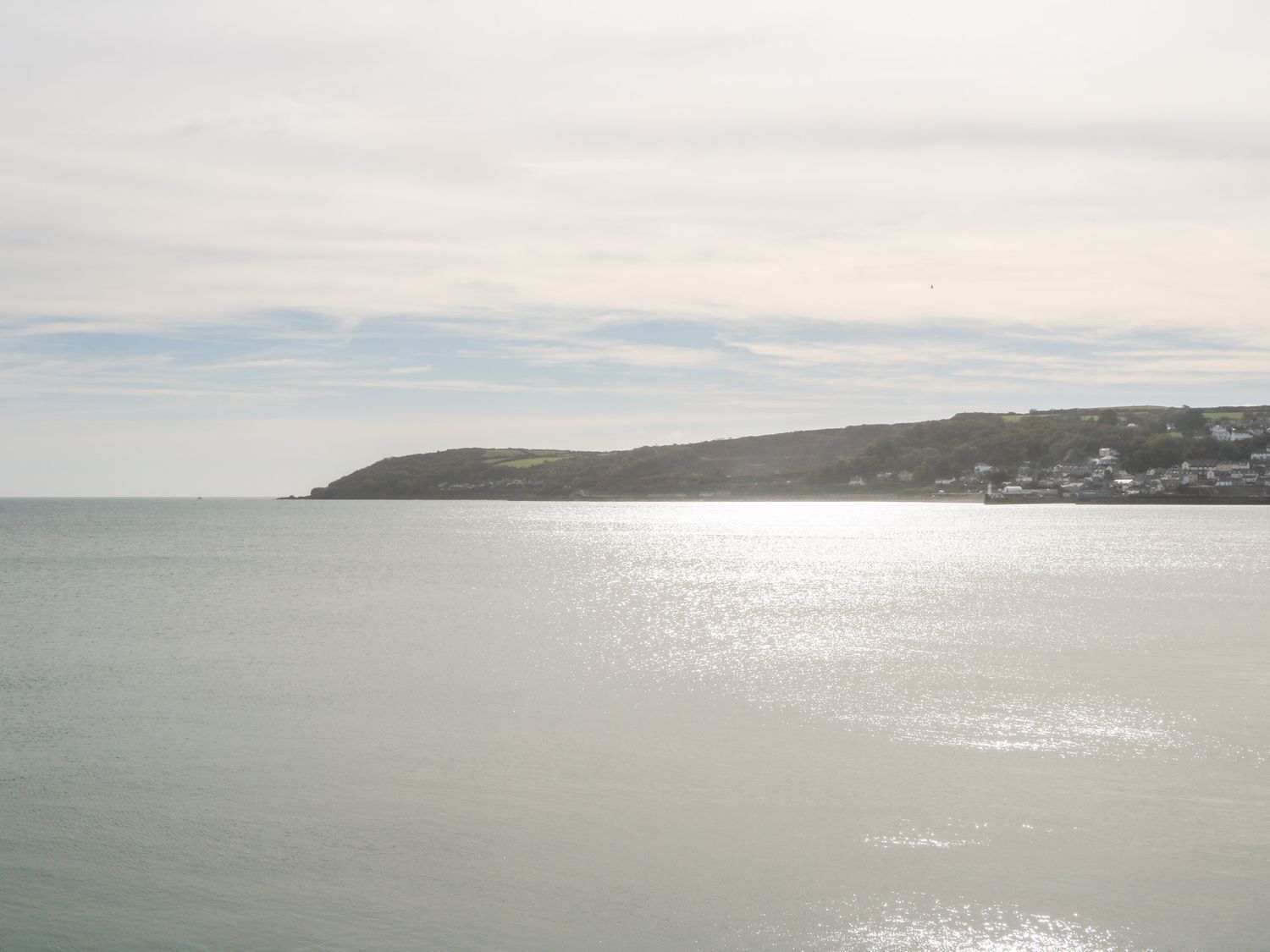 A coastal view with a calm sea, a distant hill with buildings, and a clear sky.