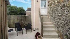 A small outdoor patio with a stone wall, a wooden fence, and a set of steps leading to a door.