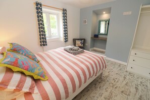 A bedroom with a bed, pillows, a window with curtains, a bedside table, a mirror, and a dresser. - Sea View Loft (Penzance)