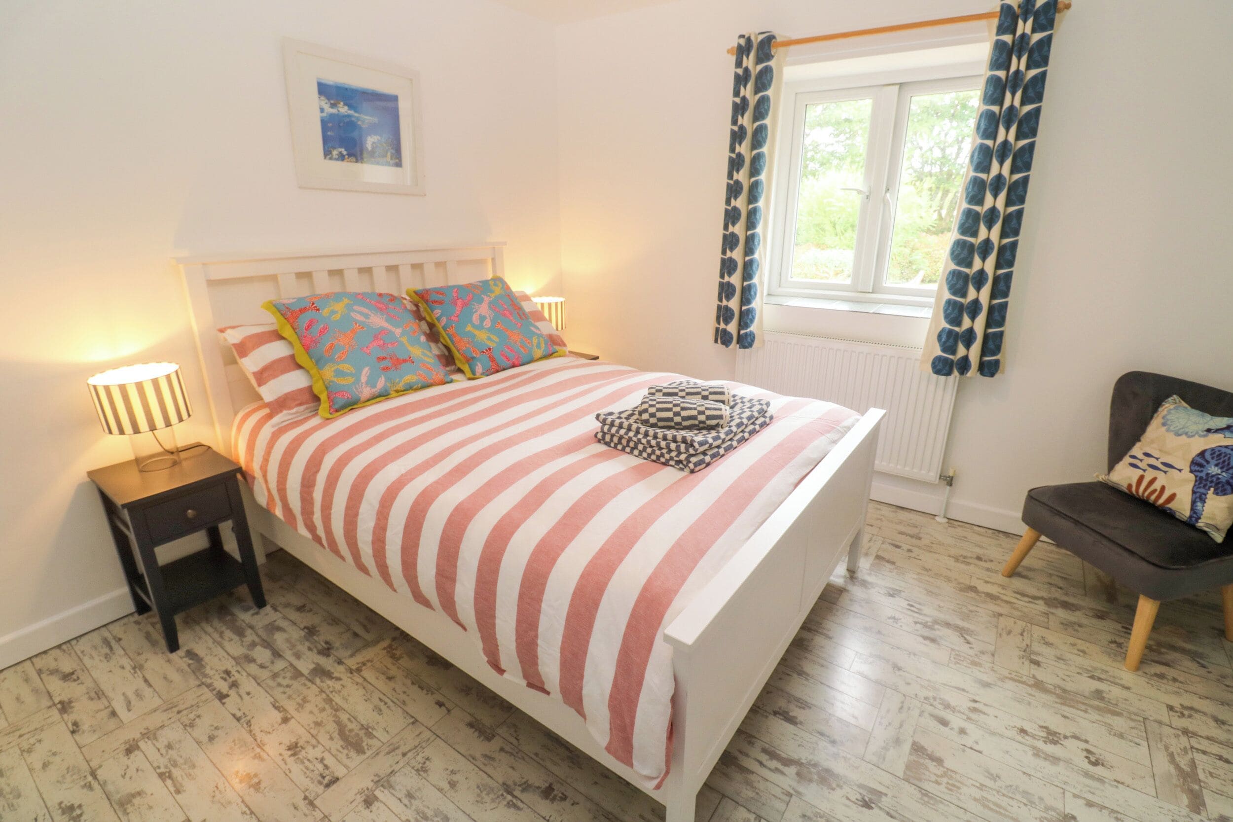 A bedroom with a bed, bedside tables, a chair, a window with curtains, and a radiator.