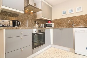 A modern kitchen with grey cabinets, a built-in oven, a microwave, and a coffee maker. - Sea View Loft (Penzance)