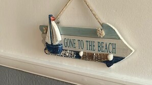 Un letrero decorativo con un velero y el texto 'GONE TO THE BEACH'.