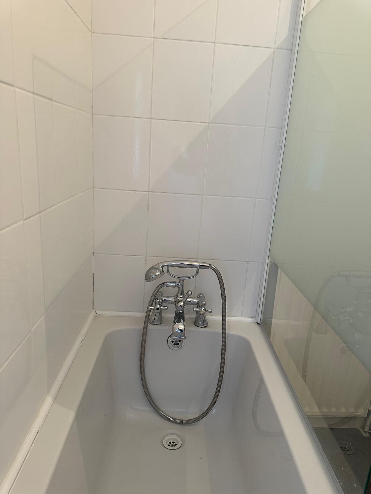 Et badeværelse med badekar, bruser og glasvæg omkring bruseren.