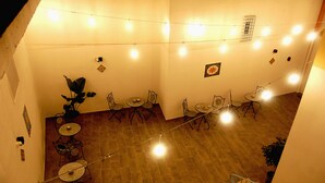 Un espace repas comprenant plusieurs tables et chaises, des guirlandes lumineuses et un escalier.