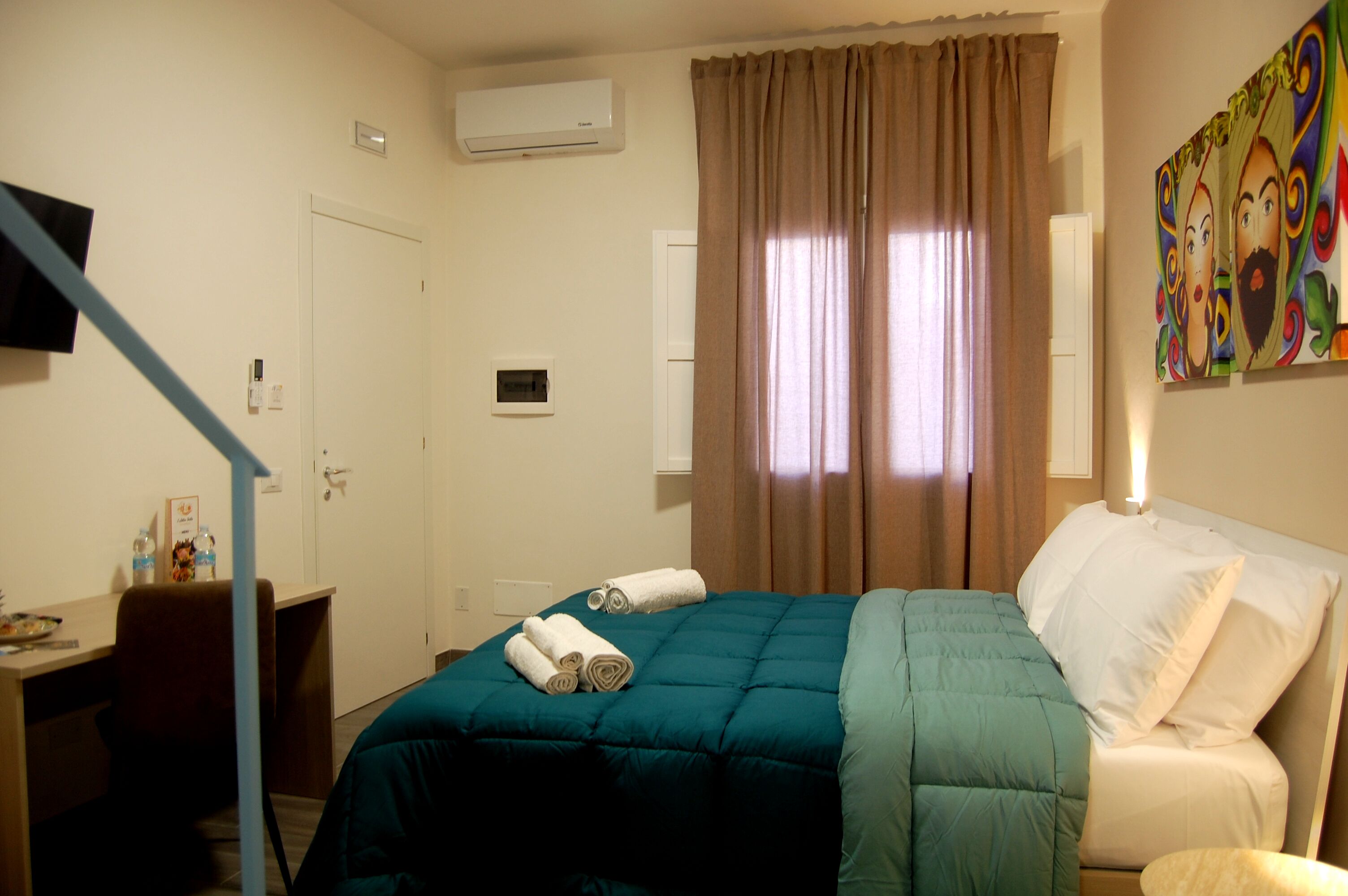 Hotelkamer met een bed, bureau, airconditioning, raam met gordijnen en een schilderij aan de muur.