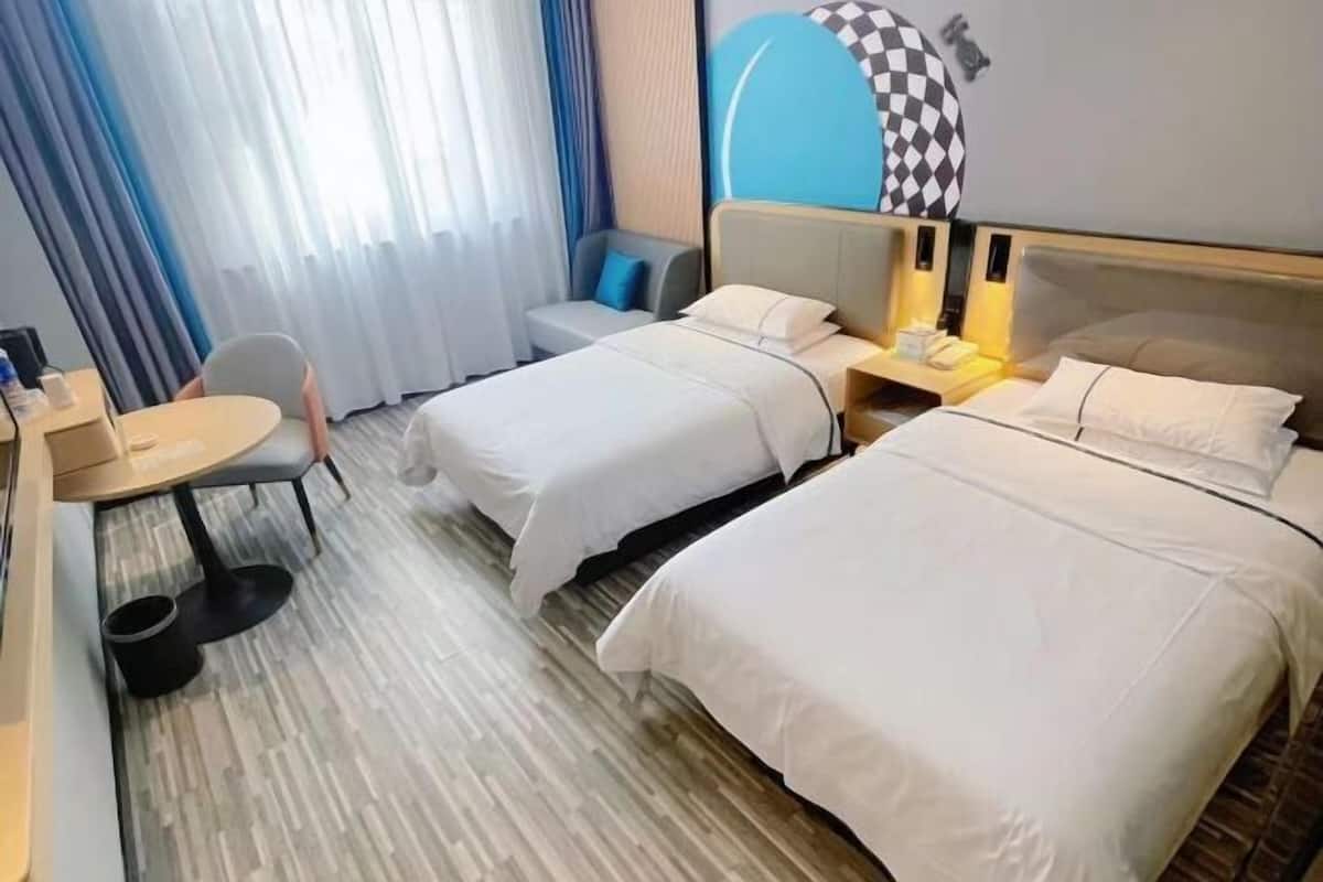 A hotel room with two beds, a small table, a chair, and a desk with a lamp.