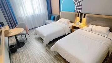 A hotel room with two beds, a small table, a chair, and a desk with a lamp.