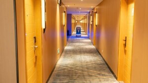 Um corredor de hotel com carpete estampado, paredes de madeira e uma mesa de recepção ao fundo.