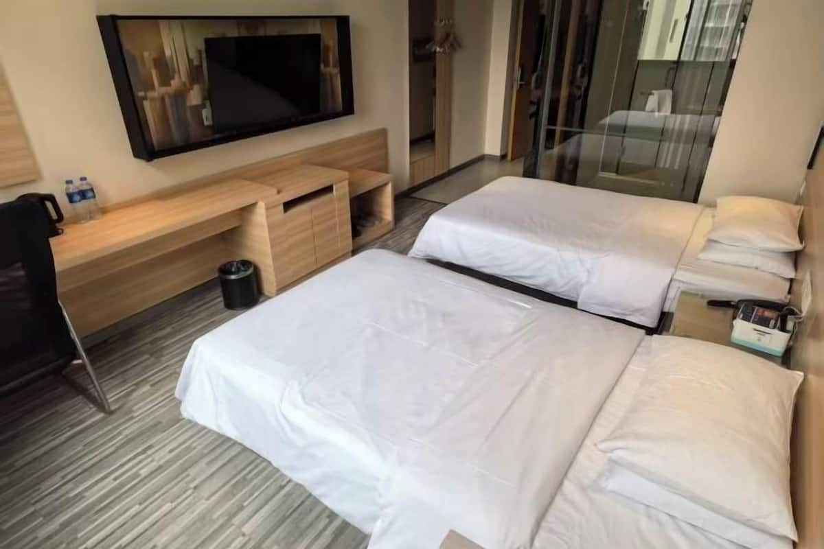 A hotel room with two beds, a TV mounted on the wall, a desk with a chair, and a trash bin.