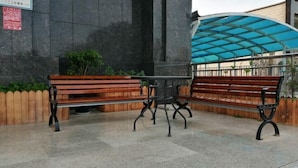 Conjunto de banco e mesa encostado em uma parede de pedra com toldo azul acima.