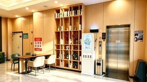 A hotel lobby with a reception desk, seating area, a large bookshelf, an elevator, and a trash bin.
