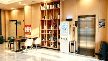 A hotel lobby with a reception desk, seating area, a bookshelf, an elevator, and a trash bin.